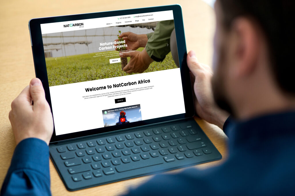 Tablet displaying the NatCarbon Africa homepage with a person planting a seedling in a greenhouse in the hero image.